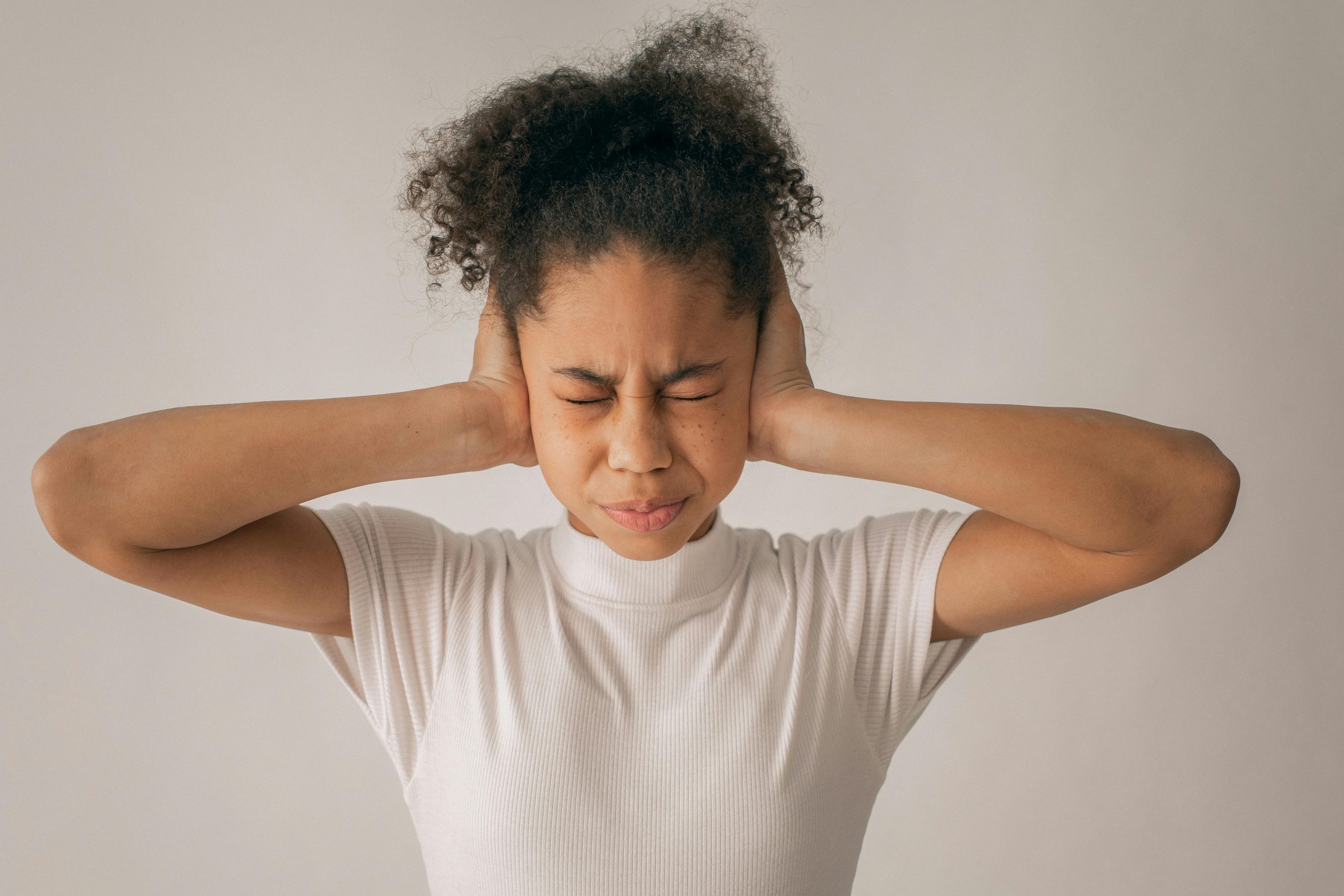 woman standing against a white wall, covering her ears