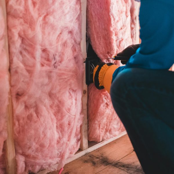man installing pink insulation material into a wall frame