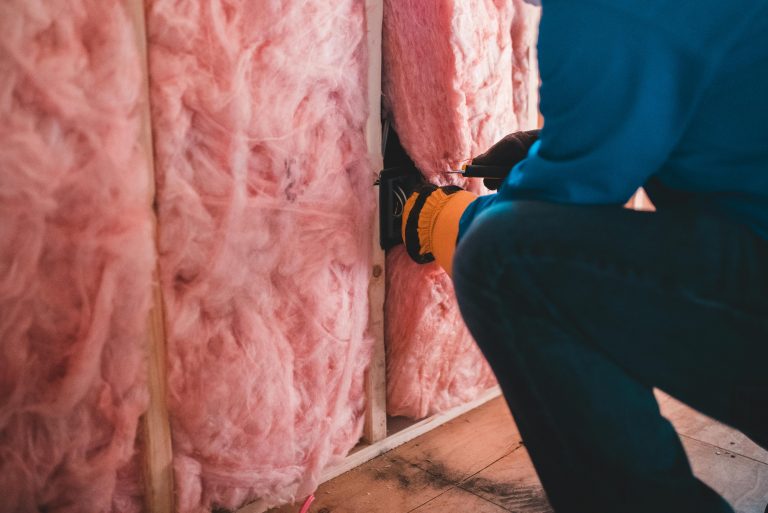 man installing pink insulation material into a wall frame