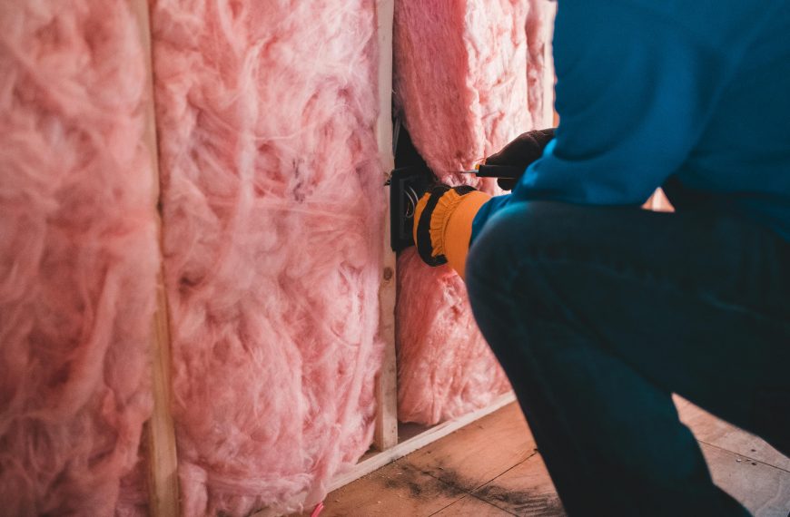 man installing pink insulation material into a wall frame
