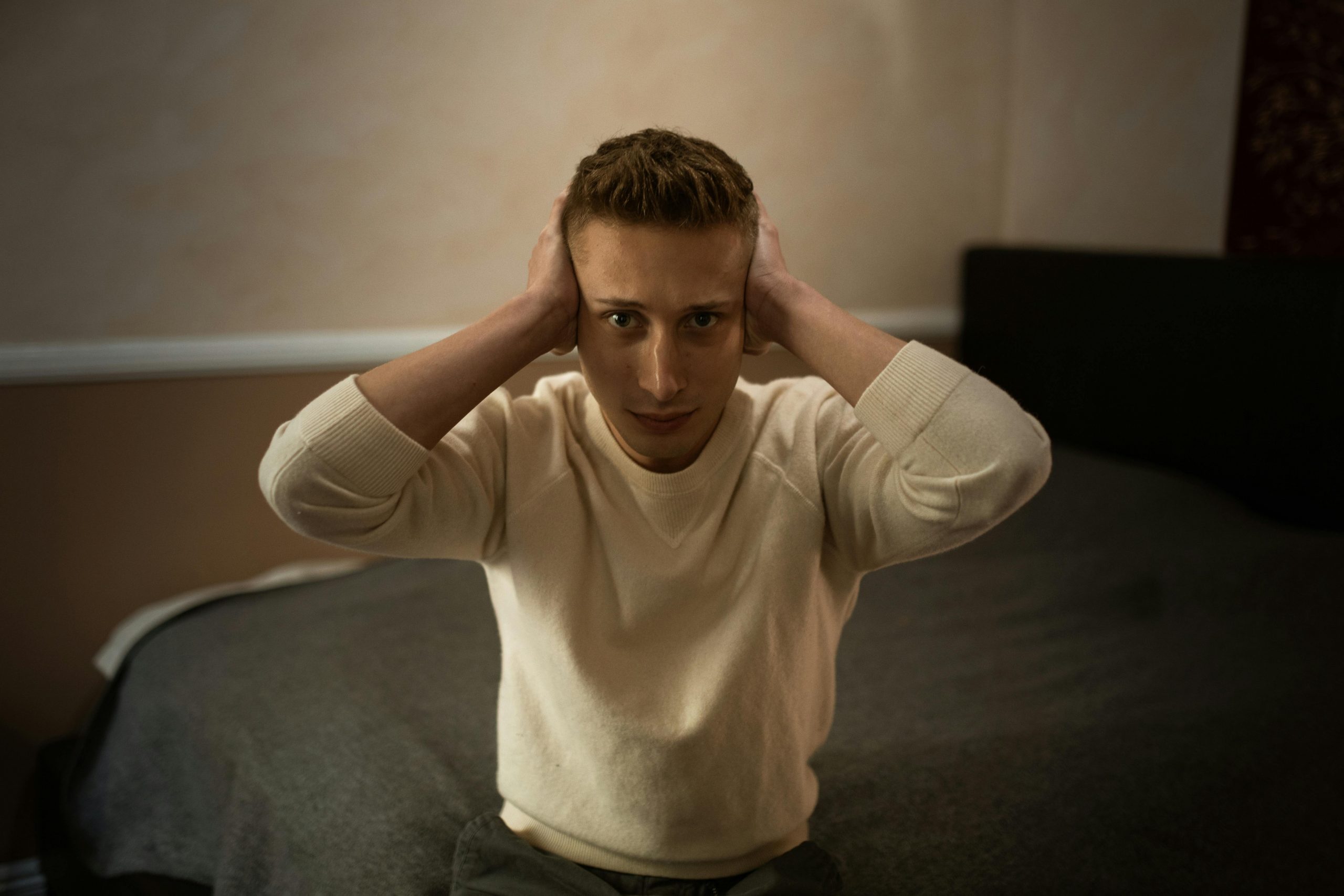 man sitting on a bed with his hands over his ears